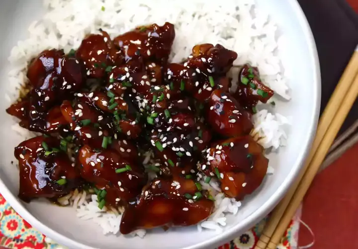En skål med fluffigt ris toppad med glaserad teriyaki kyckling, strödd med sesamfrön och gräslök.