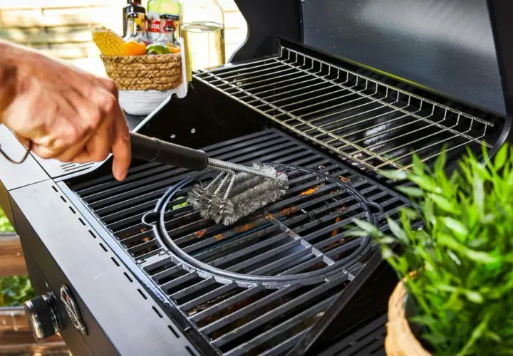 Main d'homme utilisant une brosse métallique pour nettoyer la plaque du barbecue.
