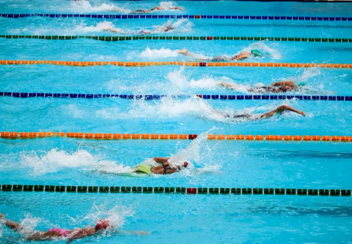 Zawodnicy w trakcie wyścigu pływackiego. Woda rozpryskuje się wokół nich, gdy wykonują ruchy. To dynamiczne sporty wodne po angielsku.