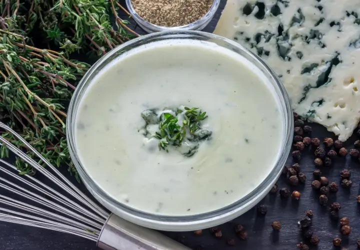 Crema suave con trozos de queso azul y tomillo fresco, lista para convertirse en una deliciosa salsa roquefort.
