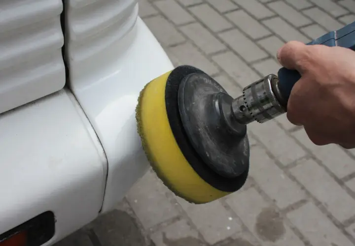 Ręka trzyma polerkę z żółtą gąbką, która jest używana do polerowania białego zderzaka. To pokazuje, jak polerować auto.