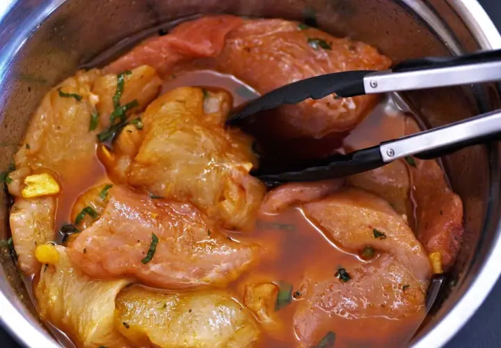 Morceaux de porc marinés dans une sauce rouge, prêts à être cuits. Une araignée de porc se cache dans la marinade.