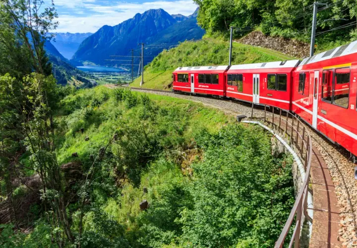 Czerwony pociąg jedzie przez malownicze szwajcarskie góry. Sprawdź swiss travel pass cena, by odkryć te widoki!