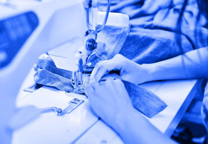 Mains guidant du tissu bleu sous une machine à coudre, un aperçu de l'industrie du vêtement en pleine action.