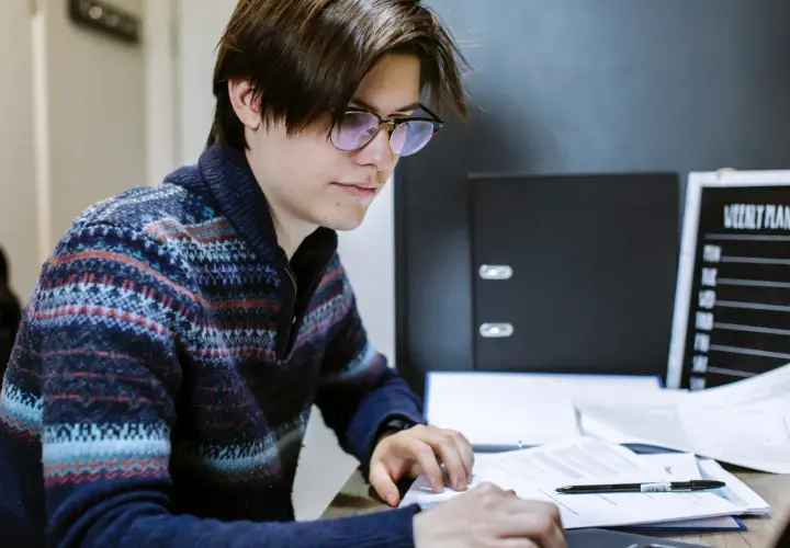 A young man with glasses studies documents, working towards his online public administration certificate.