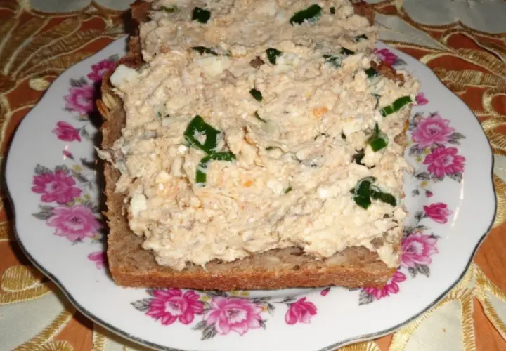 Pyszna pasta z makreli i twarogu z zieloną cebulką na ciemnym chlebie, podana na talerzu z różami.