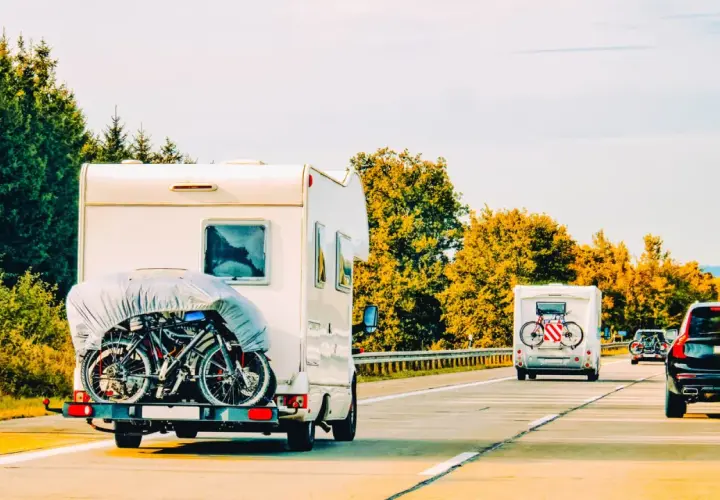 Kampery z rowerami na bagażniku jadą drogą. W tle lasy, jesienne drzewa. To widok jak z wakacji, może nawet z okolic roztocze lubelskie.