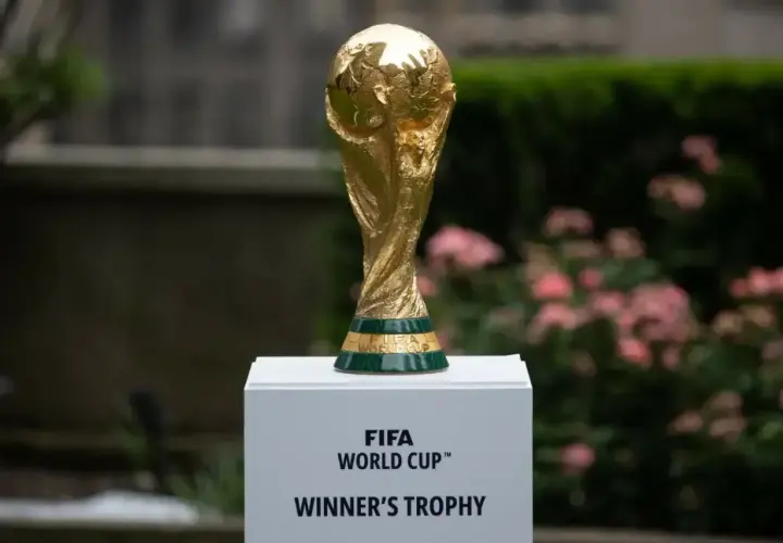 Złote trofeum FIFA World Cup, symbol zwycięstwa w mistrzostwach świata, lśni na tle zieleni i różowych kwiatów.