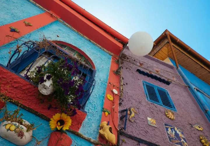 Coloratissimi edifici a Vietri sul Mare: cosa vedere? Finestre fiorite, decorazioni marine e un cielo azzurro.