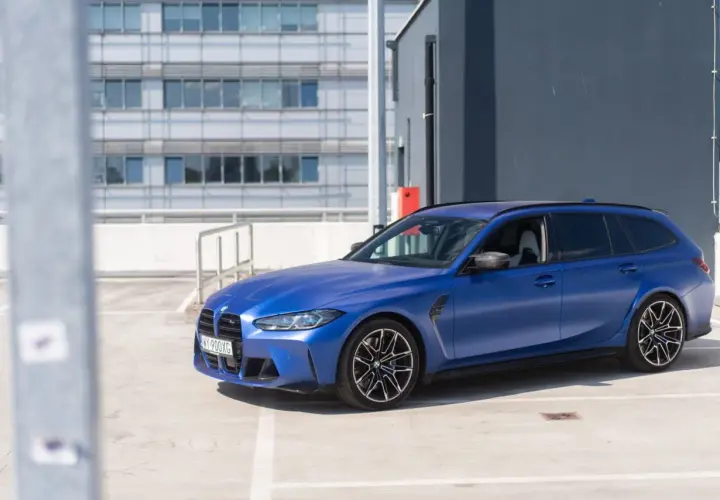 Niebieskie BMW G81 na parkingu, z nowoczesnym budynkiem w tle.