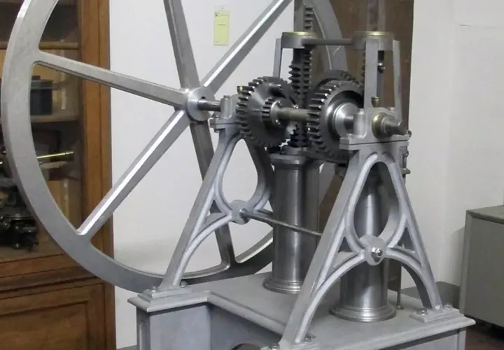 Mechanizm z kołem zamachowym i zębatkami, przypominający wczesne próby stworzenia silnika spalinowego.