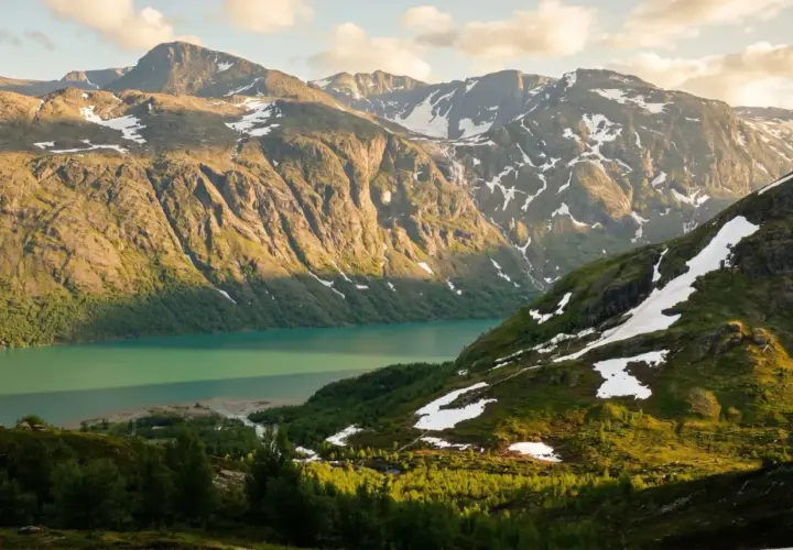 Majestatyczne góry Jotunheimen, jezioro o turkusowej barwie i zielone zbocza z resztkami śniegu.