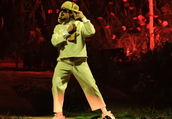 Bad Bunny w beżowym dresie i futrzanej czapce, jakby z "bad bunny café con ron tekst", tańczy na tle czerwonych kwiatów.