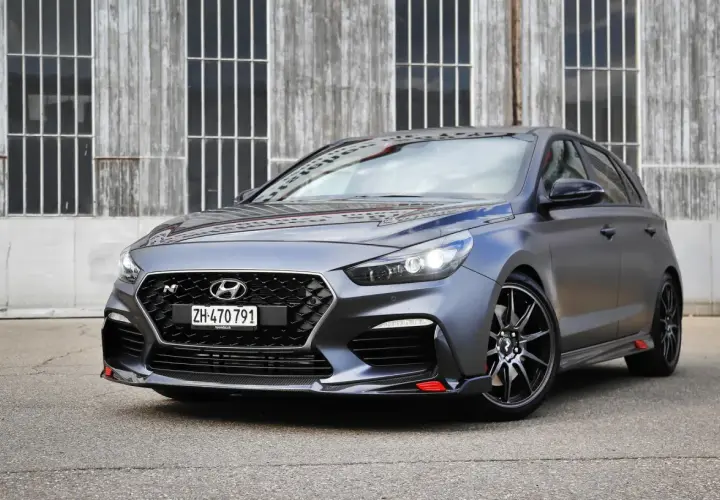 Grauer Hyundai i30 N Project C mit roten Akzenten vor Holzwand.