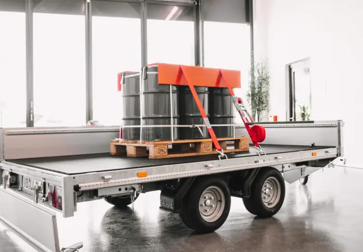 Fass auf einem Anhänger sind drei Fässer auf einer Palette sicher mit roten Gurten und einem orangefarbenen Halter frei verladen.