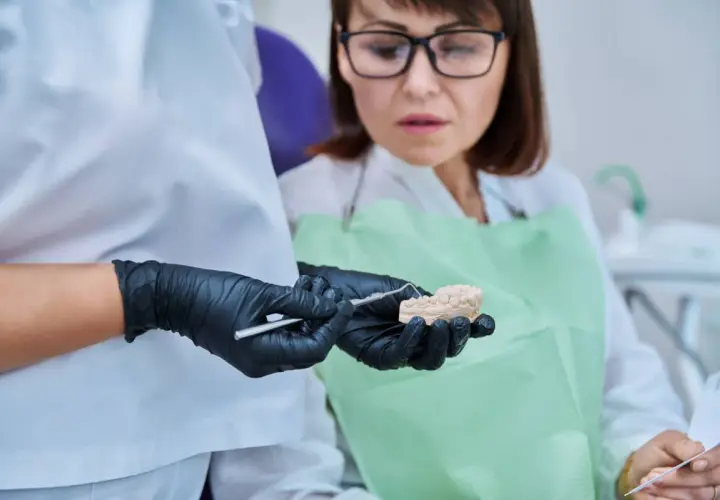 Dentysta pokazuje pacjentce model szczęki, omawiając problem połknięcia plomby amalgamatowej.