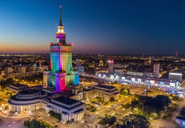 Pałac Kultury i Nauki w Warszawie, o imponującej wysokości, rozświetlony tęczowymi barwami na tle nocnego nieba.