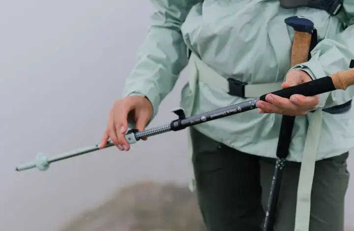 Osoba w jasnej kurtce trzyma kijki trekkingowe Black Diamond Trail. Mglisty krajobraz w tle.