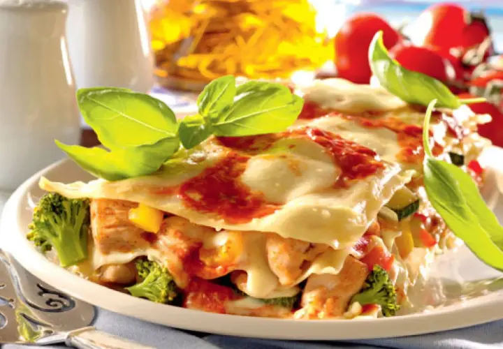 Pyszne lasagne z kurczakiem, brokułami i pomidorami, udekorowane świeżą bazylią.