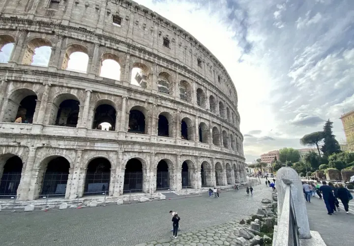 Vue extérieure du Colisée, monument emblématique de Rome. Des touristes profitent de leur visite colisée sous un ciel nuageux.
