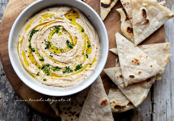 Cremoso hummus di fagioli, condito con olio d'oliva e prezzemolo, servito con pane pita tostato.