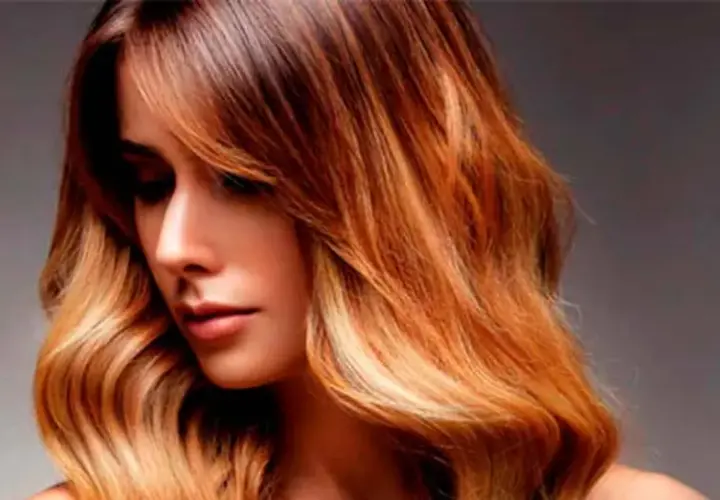 Mujer con pelo californianas, con ondas y un degradado de color castaño a rubio dorado, luciendo un estilo moderno y radiante.