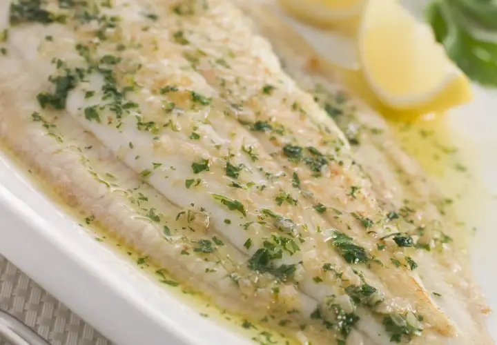 Sogliola alla mugnaia succulenta, cosparsa di prezzemolo fresco e servita con spicchi di limone.