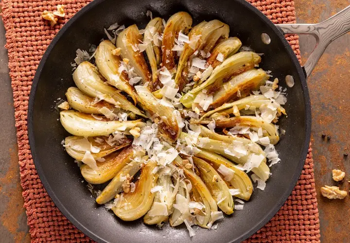 Finoçchi gratinati in padella, dorati e saporiti, guarniti con scaglie di formaggio e noci croccanti.