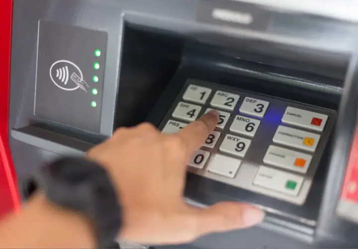 Une main tape un code sur un clavier de distributeur. Comment retrouver son code de carte bancaire ? La sécurité avant tout.