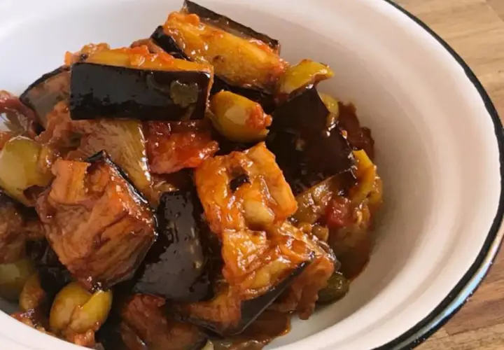 Caponata que es: un delicioso guiso siciliano de berenjenas, aceitunas y tomate, servido en un cuenco blanco.