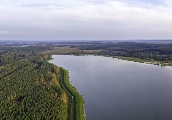 Rozległy zalew Biszcza otoczony lasem i zielonymi łąkami. Spokojna tafla wody odbija niebo.