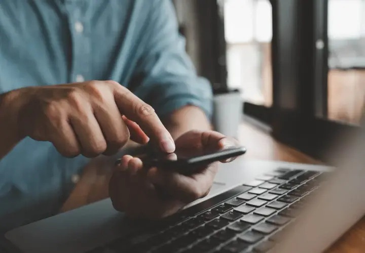 Mężczyzna sprawdza na telefonie, czy lokator może zawrzeć umowę na prąd, obok leży laptop.