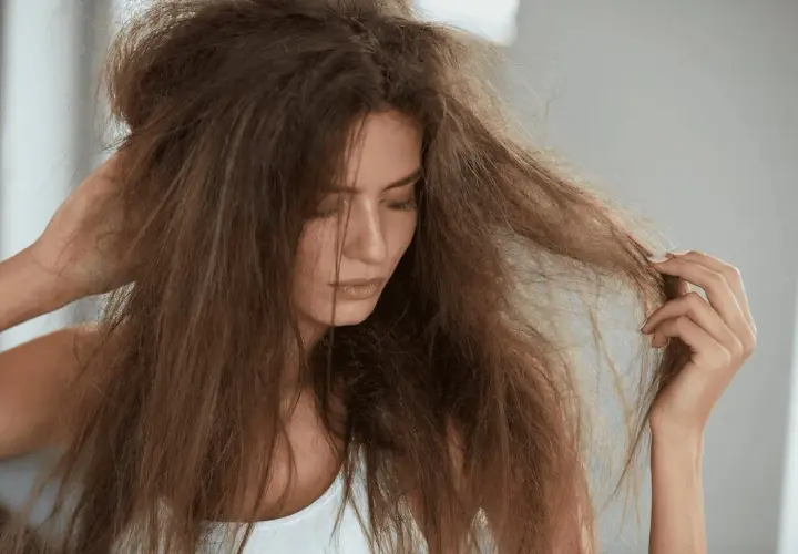 Mujer con pelo estropajo, enredado y seco, tocándose la cabeza con la mano.