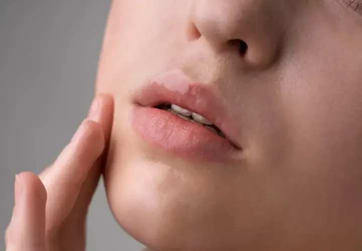 Labios rosados y brillantes, con una textura que podría sugerir la presencia de hongos en los labios, tocados suavemente por un dedo.