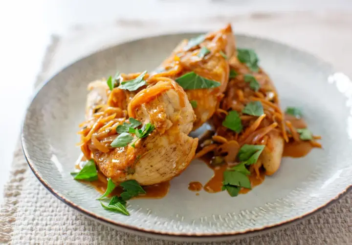 Délicieux sauté de poulet servi sur une assiette, garni d'oignons caramélisés et de persil frais.