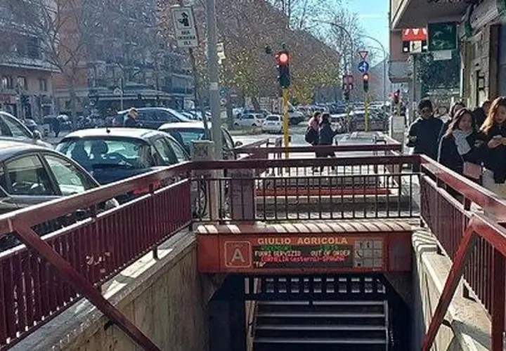 Ingresso della fermata Giulio Agricola della metro A, con persone che camminano e traffico in strada.
