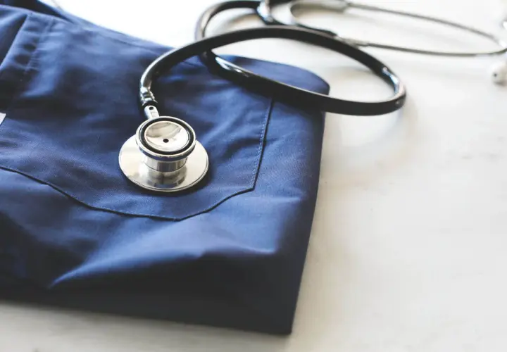 Un camice blu e uno stetoscopio appoggiati su un piano bianco. Immagine evocativa per chi vuole capire come diventare guardia medica.