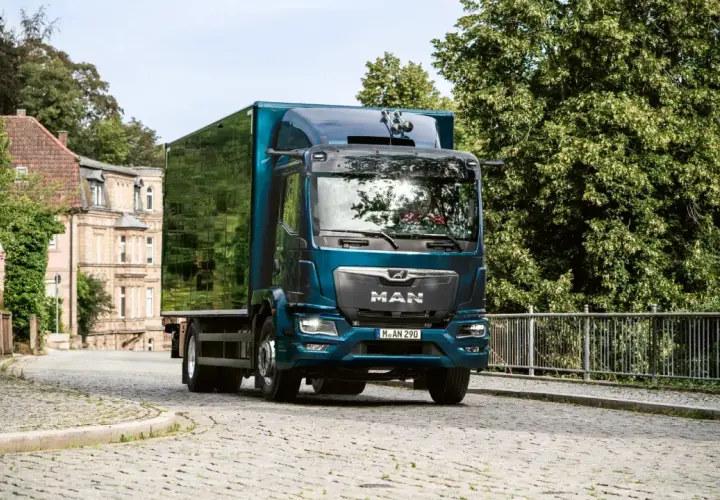 Camion MAN bleu turquoise avec remorque verte sur une route pavée.