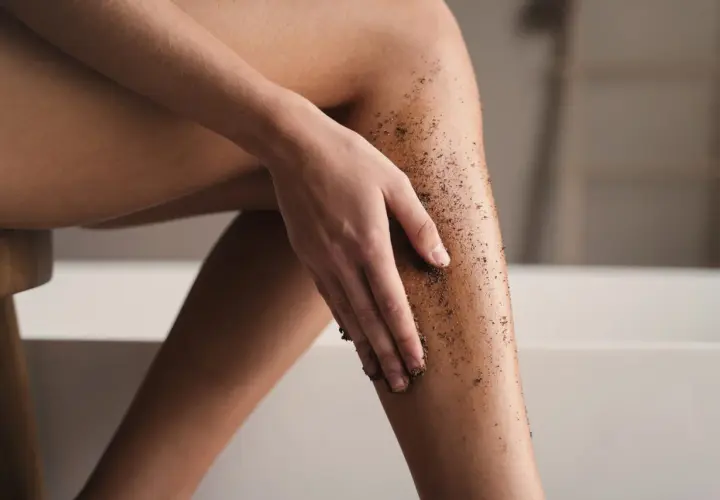 Kobieta wykonuje peeling kawowy na nogach, przygotowując skórę do golenia.