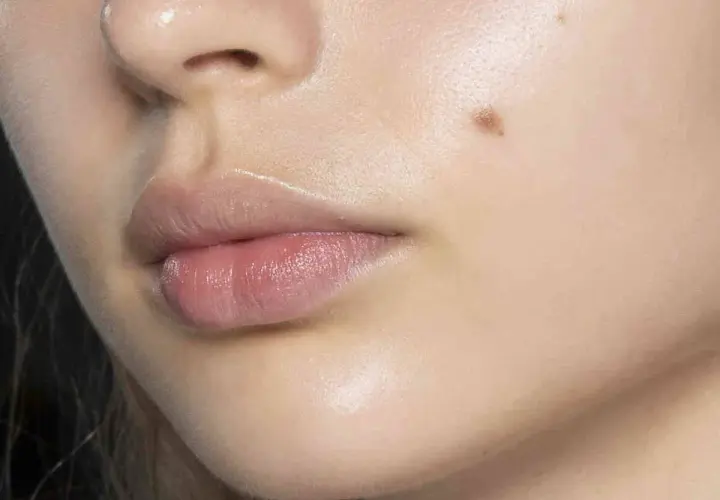 Labios rosados y piel luminosa con un lunar y un ligero vello facial.