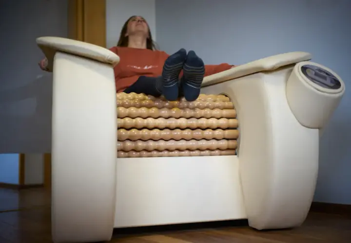 Kobieta relaksuje się na fotelu z masażem rolletic. Drewniane rolki masują jej nogi, podczas gdy ona unosi głowę do góry.
