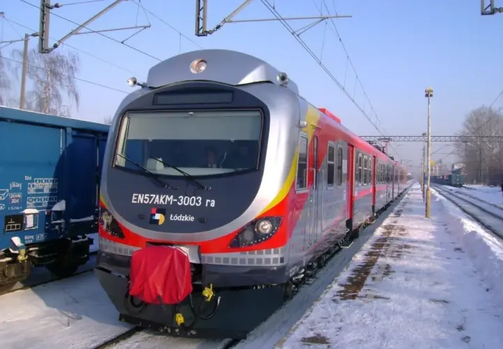 Pociąg EN57AKM-3003 ra z Łodzi stoi na zaśnieżonym peronie. Obok niebieski wagon towarowy.