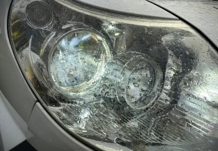 Krople deszczu na reflektorze, który świeci, sugerują jazda bez jednego światła.