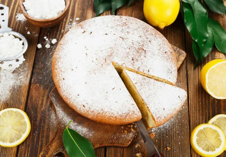 Un délicieux gâteau italien au limoncello, saupoudré de sucre glace, avec des citrons frais et des feuilles vertes sur fond de bois.