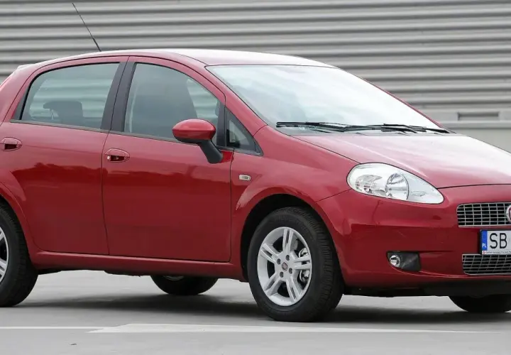 Czerwony Fiat Punto Grande z tablicą rejestracyjną SB 2823E zaparkowany na szarym podłożu.