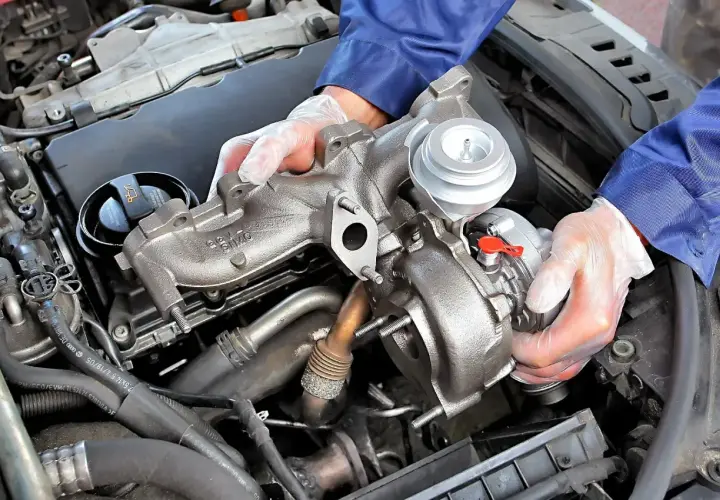 Mechanik w rękawiczkach trzyma turbosprężarkę. Uszkodzony czujnik doładowania turbiny objawy mogą być różne, ale często wiążą się z utratą mocy.