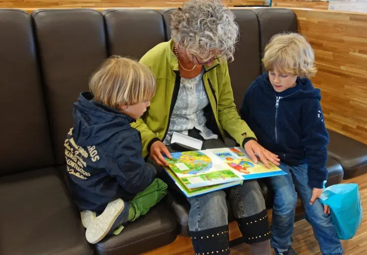 Oma und Enkel sitzen auf einer Bank und lesen gemeinsam ein buntes Bilderbuch.