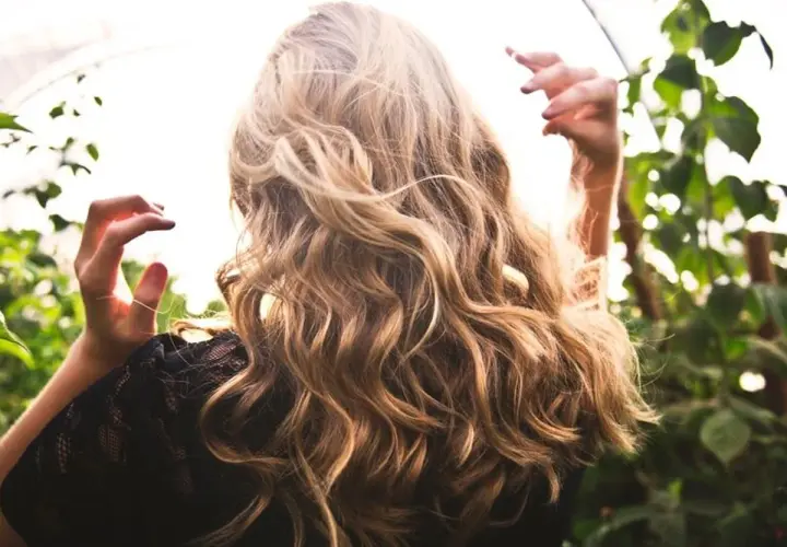 Cabello rubio con reflejos naturales, como si fuera babylights vs balayage. Manos en el aire, rodeada de vegetación.