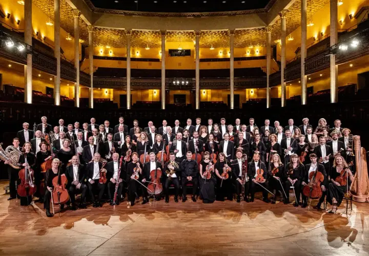 Kungliga Filharmonikerna medlemmar poserar med sina instrument i en storslagen konsertsal.