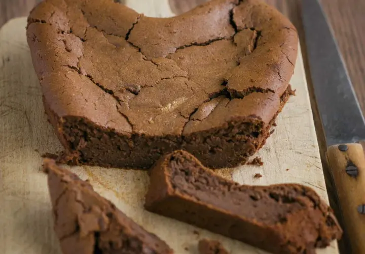 Un délicieux gâteau au chocolat en forme de cœur, un gâteau sans oeuf, craquelé sur le dessus, avec une part coupée.